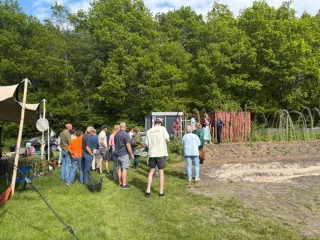 Een groep mensen die staan te luisteren naar een spreker in de sociale voedseltuin